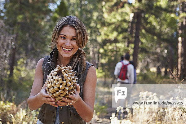 Portrait of young woman in forest holding large pine cone  Los Angeles  California  USA