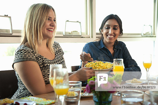 Gruppe von Freunden beim Essen am Tisch  junge Frau gibt Teller an Freund weiter