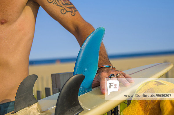 Ausschnitt eines reifen männlichen Surfers  der das Surfbrett am Strand vorbereitet.