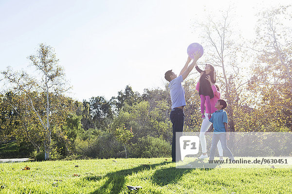 Mature couple and children playing catch with ball in park