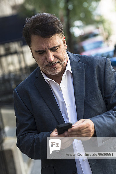 Reife Geschäftsleute gehen auf der Straße SMS auf dem Smartphone