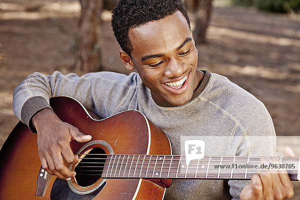 Junger Mann sitzt im Wald und spielt Akustikgitarre.