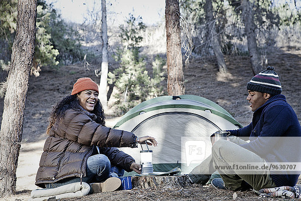 Junges Camping-Paar im Wald sitzend  lachend und plaudernd