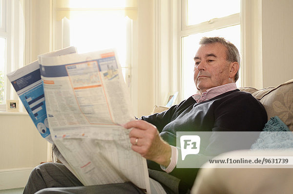 Senior im Sessel sitzend Zeitung lesen