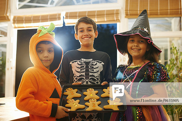 Brüder und Schwestern in Halloween-Kostümen halten Tablett mit Lebkuchenmännern