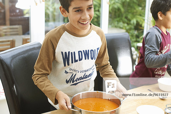 Jungen am Küchentisch mit Tomatensuppe in der Pfanne
