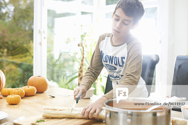 Junge kocht Baguette und Kürbissuppe in der Küche