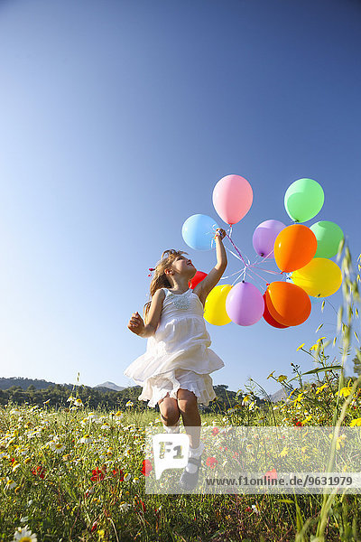 Mädchen springen vor Freude mit bunten Luftballons auf der Wildblumenwiese  Mallorca  Spanien