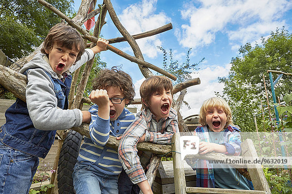 Vier Jungen schreien auf hausgemachtem Klettergerüst im Garten
