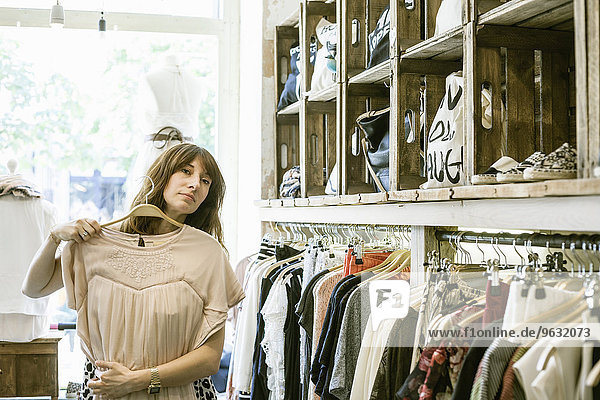 Mittlere erwachsene Frau hält Kleid vor sich in Vintage-Boutique