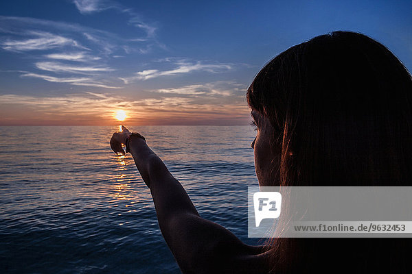 Silhouette einer jungen Frau  die auf den Sonnenuntergang vom Strand aus zeigt  Oristano  Sardinien  Italien