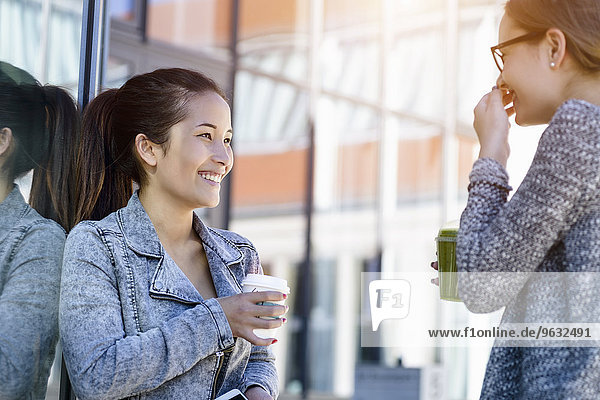 Zwei junge Frauen mit Kaffee zum Mitnehmen lachend