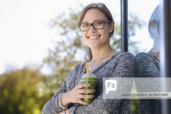 Porträt einer jungen Frau mit Kaffee zum Mitnehmen  die sich gegen das Parkgebäude lehnt