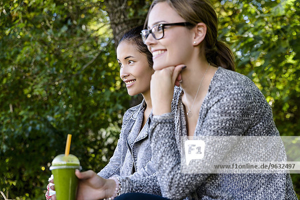 Zwei junge Frauen mit Kaffee zum Mitnehmen sitzend im Park