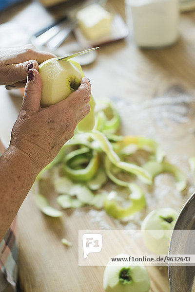 A woman peeling a green skinned apple.