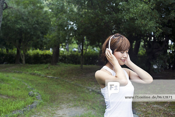 A woman in a Kyoto park  wearing headphones. Wearing jogging kit.