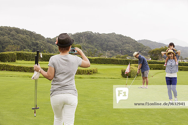 Family on a golf course.A child and three adults. a woman with a camera.