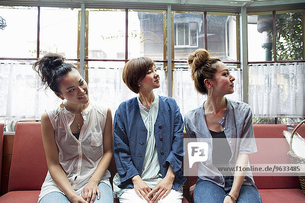 Three women sitting indoors on a bench  looking away.