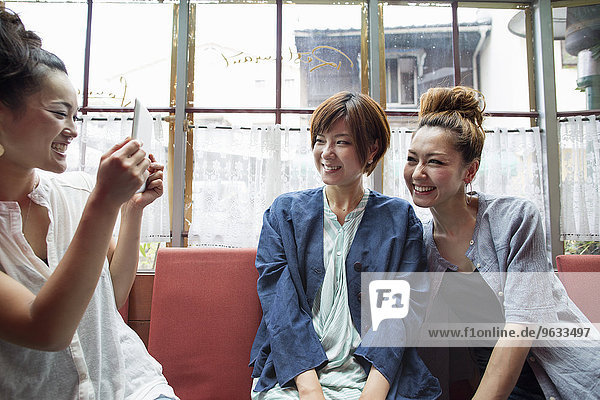 Three women sitting indoors  one holding a digital tablet  taking picture.