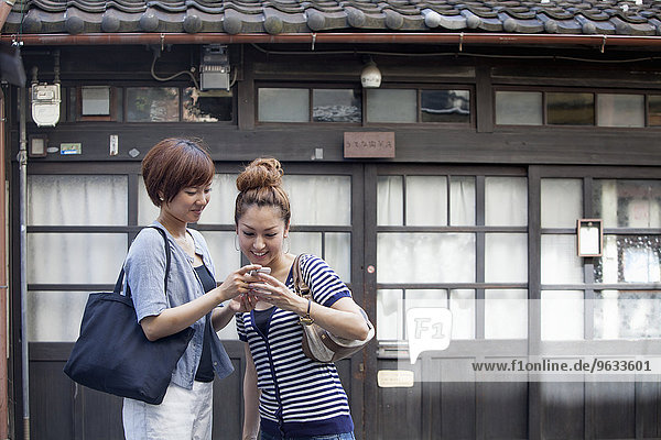 Two women standing outdoors  looking at cellphone.