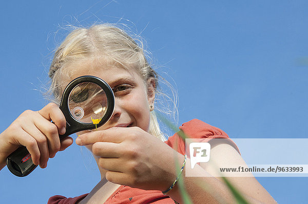 Girl (10-11) examining flower through magnifying glass  low angle view  close-up