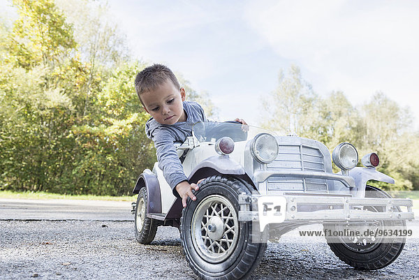 Portrait small boy checking tire model vintage car