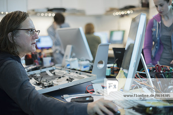 A man seated at a computer  looking at the screen. Computer repair shop.