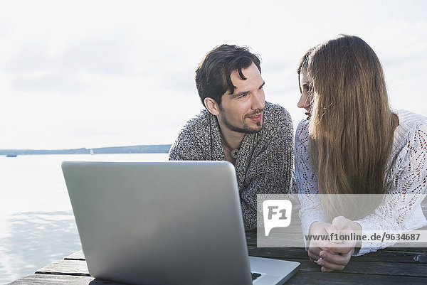 Young couple wooden jetty laptop computer