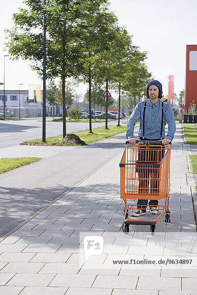 Young man woollen hat pushing shopping trolley