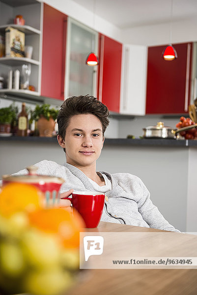 Young man sitting with a cup in his hands at the kitchen table