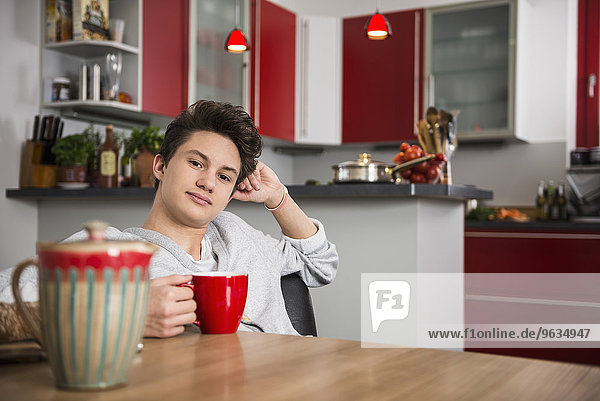 Young man sitting with a cup in his hands at the kitchen table