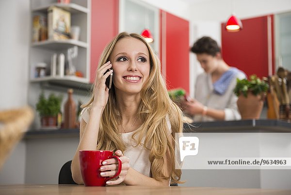 Teenager girl talking on mobile phone with man in the background at the kitchen table