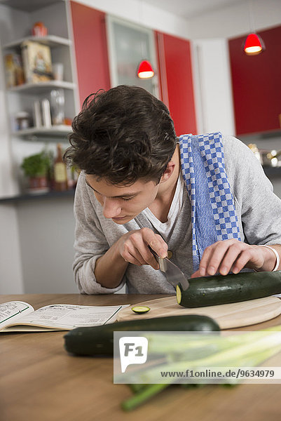 Young man helping recipe book with preparing food in kitchen