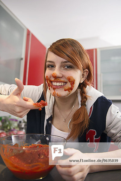 Happy young woman eating tomato sauce in kitchen