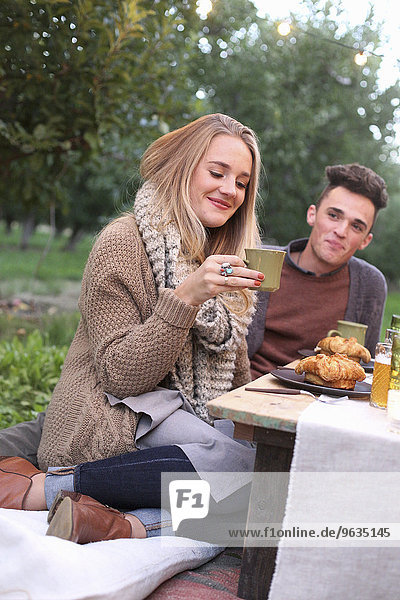 An apple orchard in Utah. A couple sitting on the ground  food and drink on a table.
