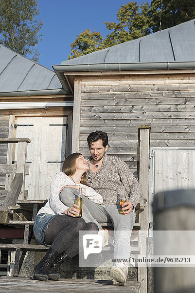Young couple sitting boathouse jetty drinking beer