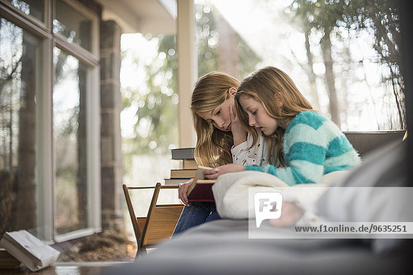 Two girls sitting on a sofa  reading a book.