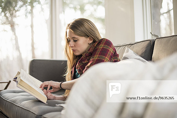 Young woman lying on a sofa  reading a book.