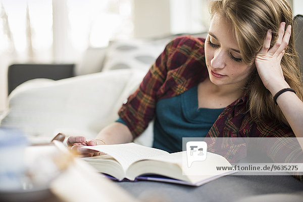Young woman sitting on a sofa  reading a book.