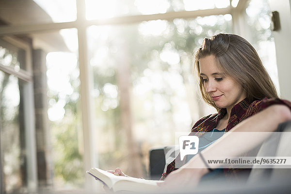 Smiling woman sitting on a sofa  reading a book.