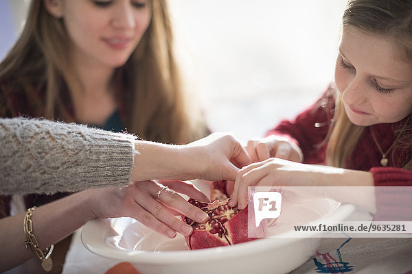 Two girls and a woman sitting at a table  picking kernels from a pomegranate.