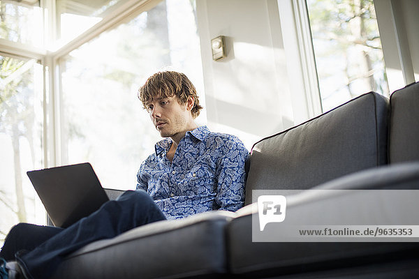 Low angle view of a man sitting on a sofa looking at his laptop.