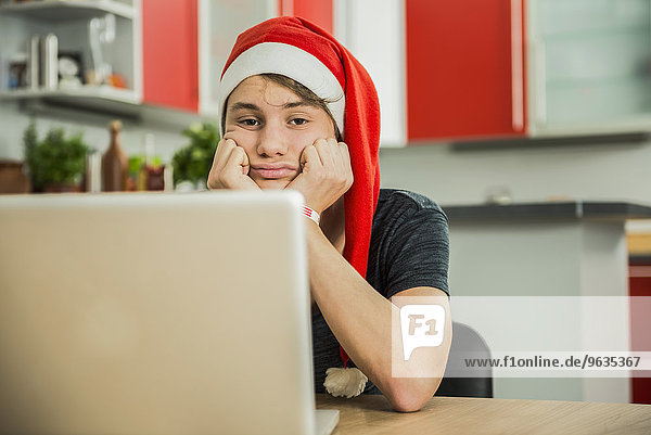 Bored young man with Santa hat using laptop