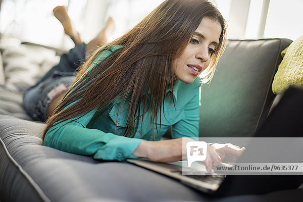 Woman lying on a sofa looking at her laptop  smiling.