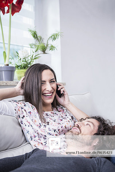 Woman talking on mobile phone with her husband lying on lap