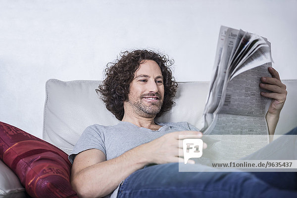 Man lying down on couch and reading a newspaper