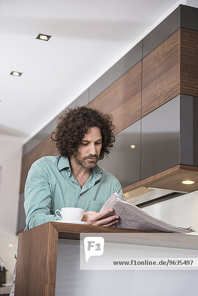 Man sitting in a kitchen and reading a newspaper