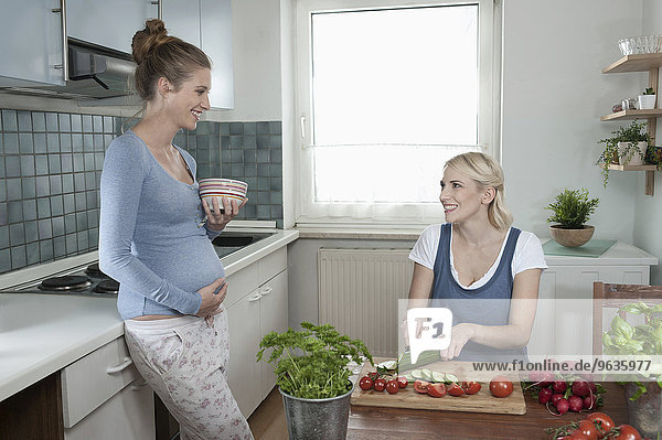 Two young woman pregnant kitchen talking cooking