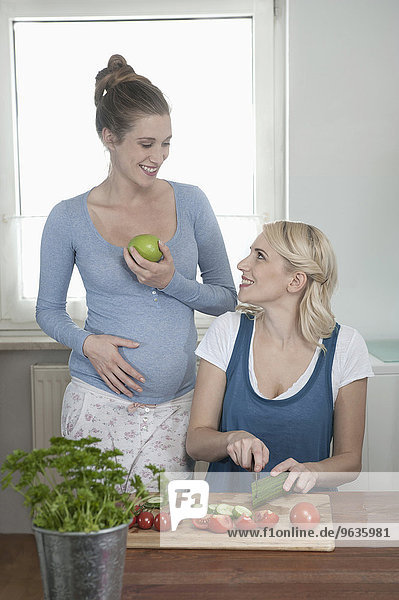 Two young women kitchen salad talking smiling