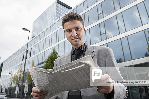 Businessman reading a newspaper outside office building